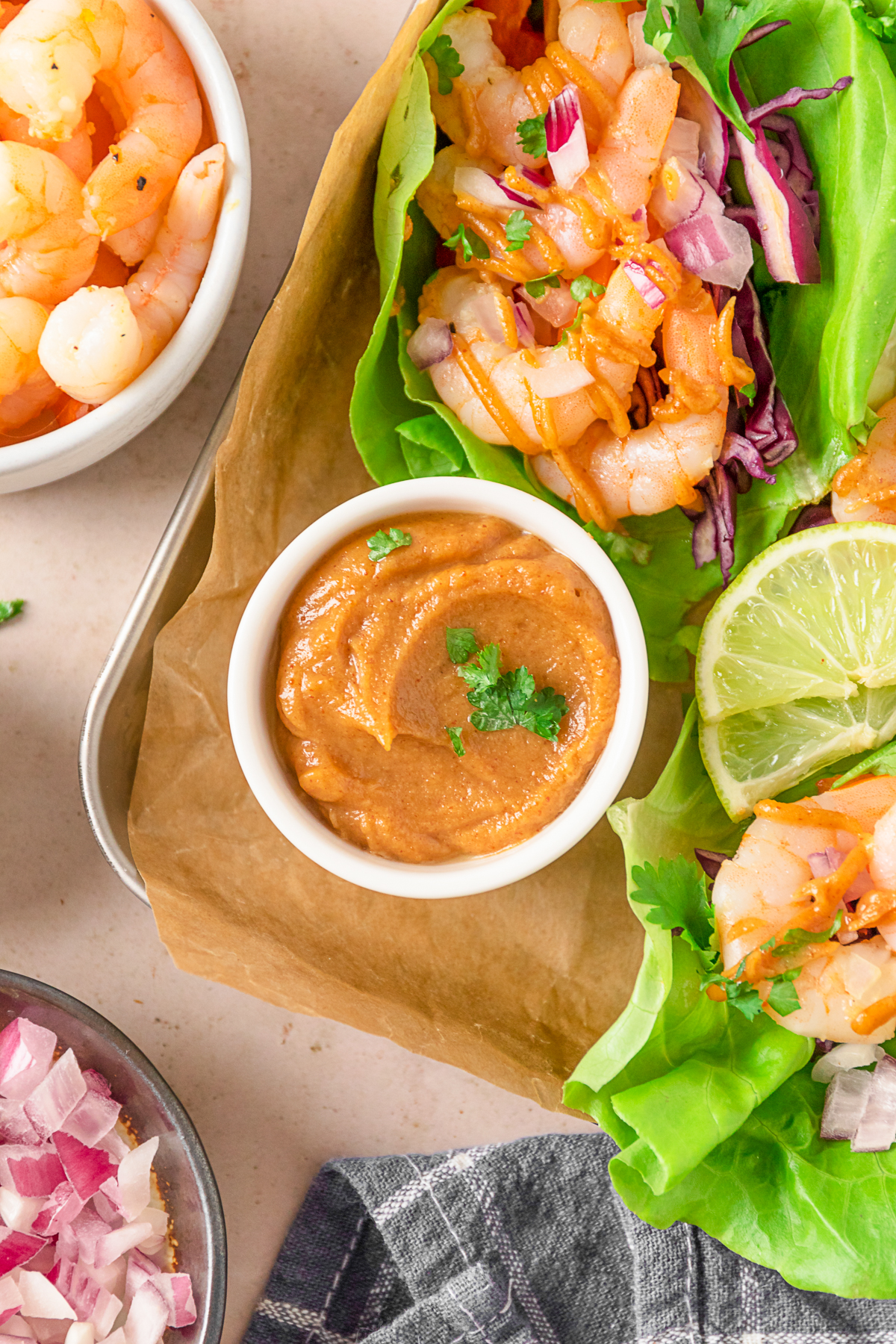 Peanut sauce in a dipping bowl surrounded by shrimp wraps. 
