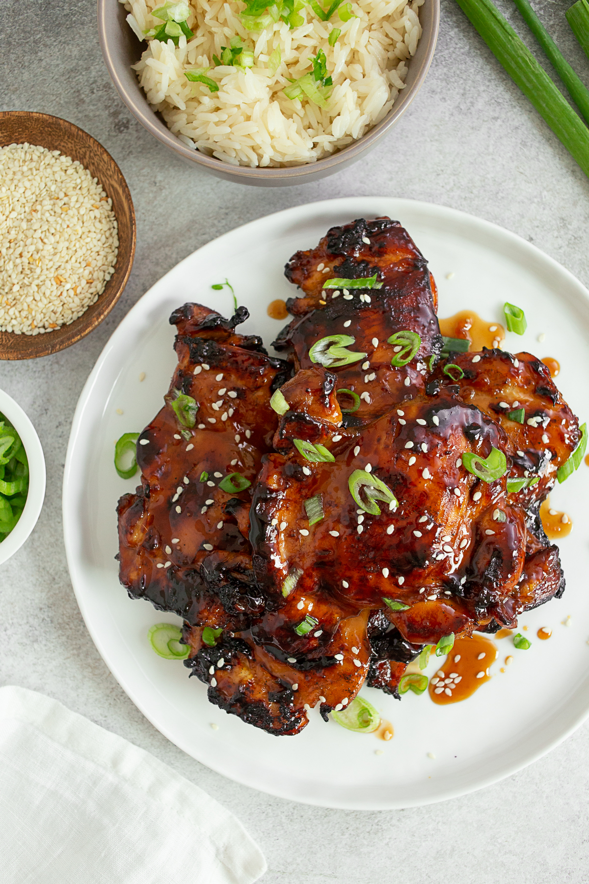Grilled Teriyaki Chicken on a white plate topped with sesame seeds and green onions. 