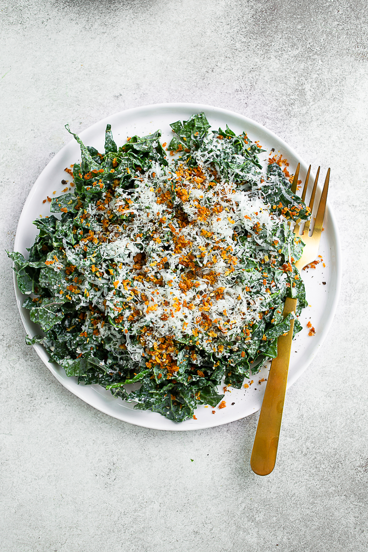 Chopped Kale Caesar Salad on a round white plate with a gold fork. 