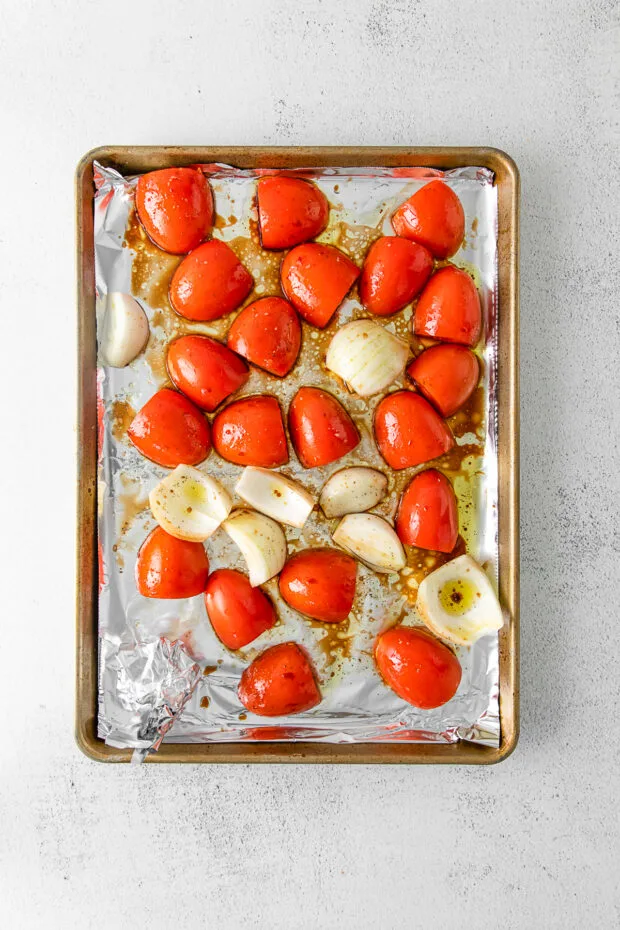 Uncooked tomatoes and onions on a sheet pan. 