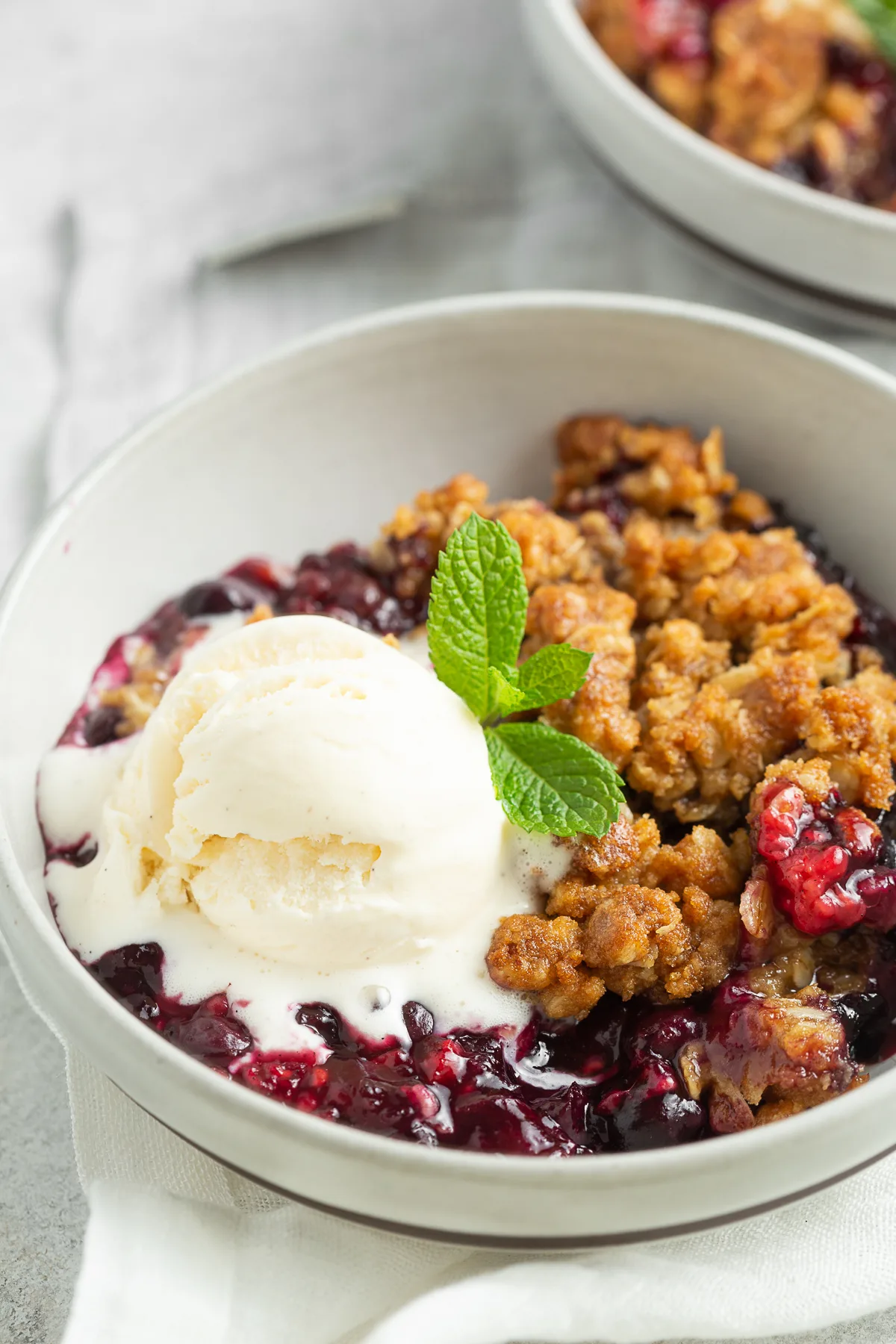 Triple Berry Crisp in a bowl with ice cream and mint. 