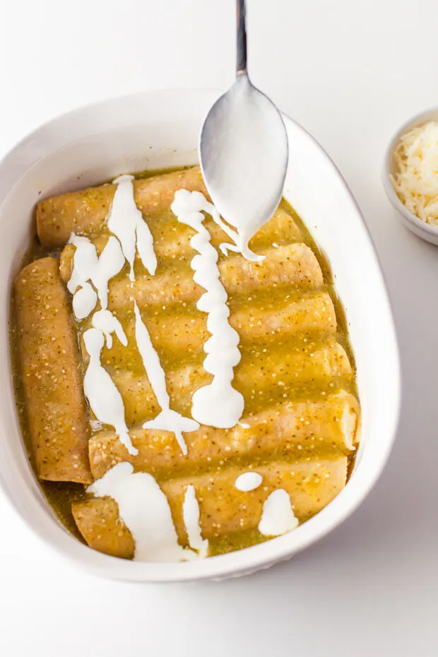 Sour cream getting drizzled over enchiladas. 