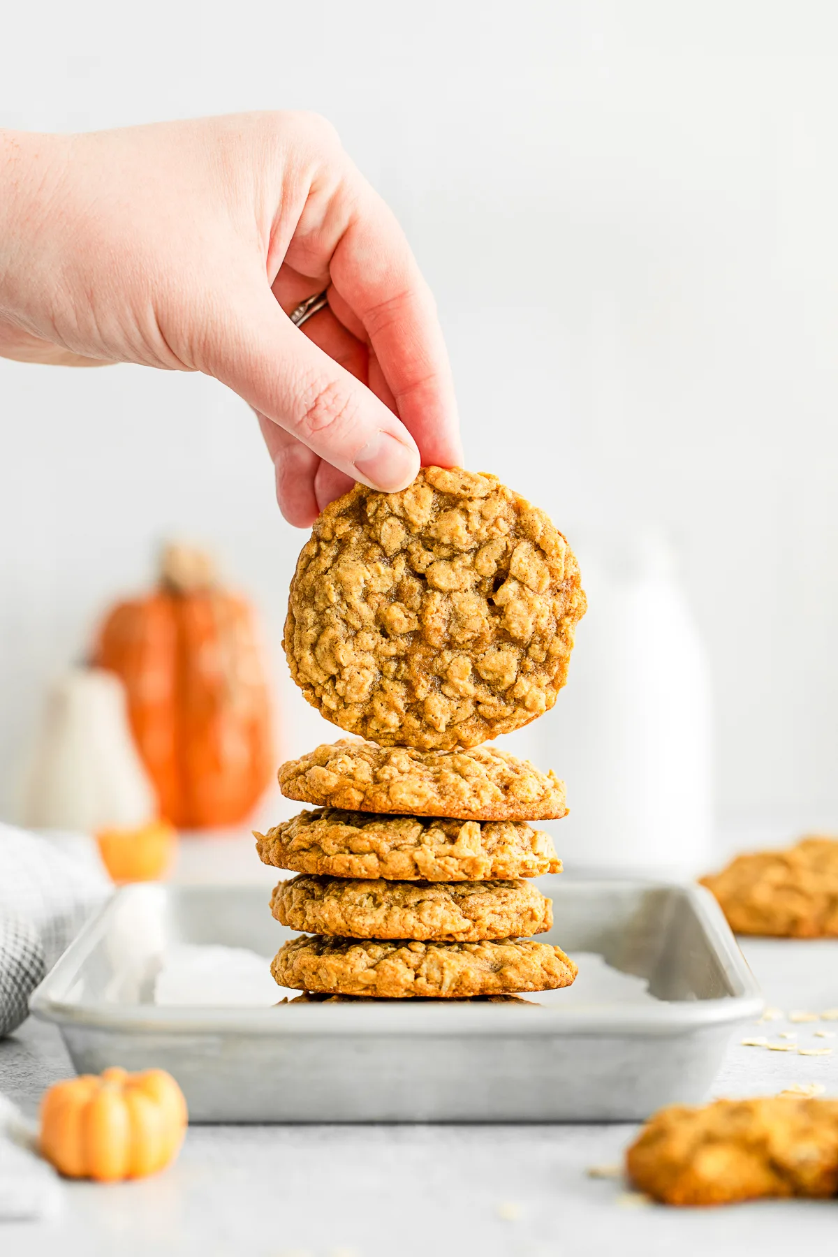 Stacked Pumpkin Oatmeal Cookies on a sheet pan with a hand holding one of the cookies. 