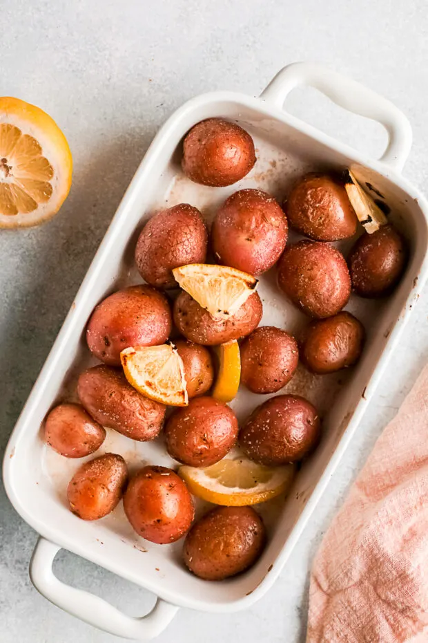 Whole roasted red potatoes with lemons in a white dish. 