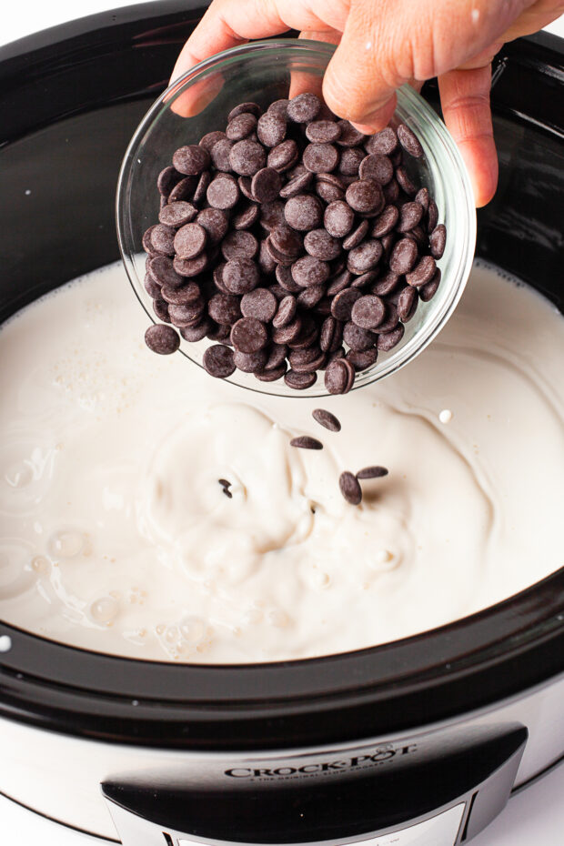 Pouring chocolate chips into milk in a slow cooker.