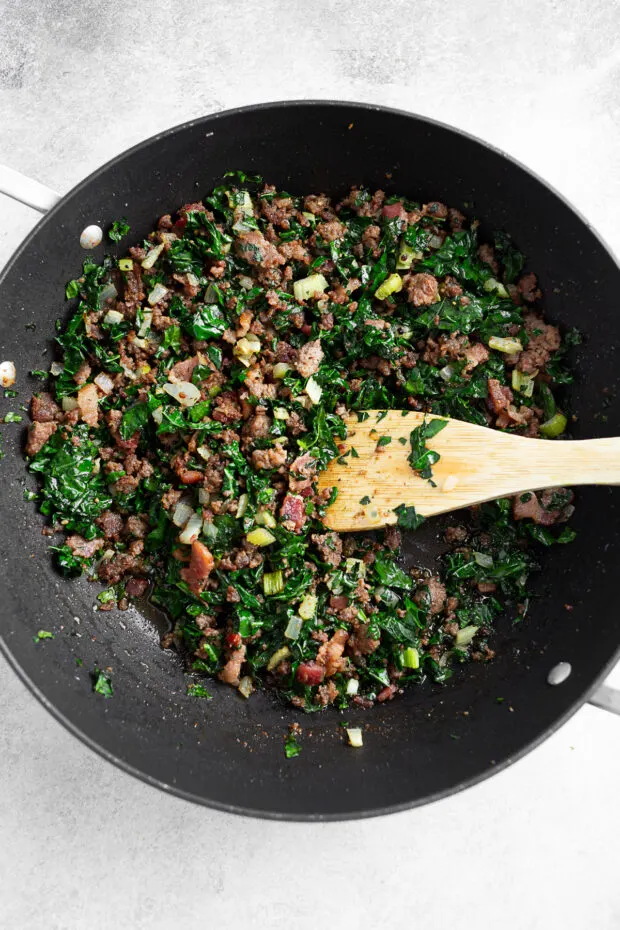 Sautéed sausage, bacon, and kale in a skillet. 