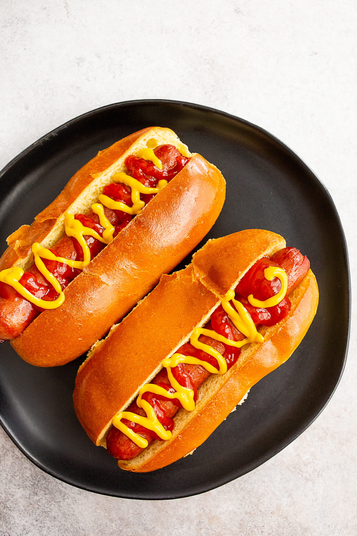 2 air fryer cooked hot dogs sitting on a plate with mustard and ketchup.