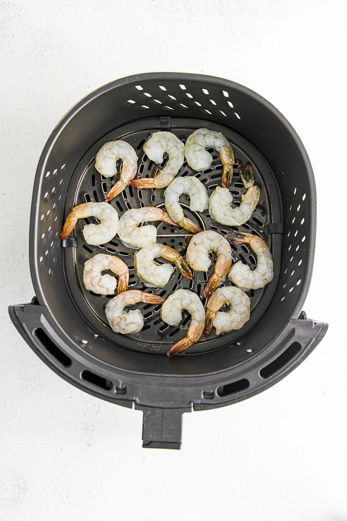 Uncooked shrimp in an air fryer basket. 