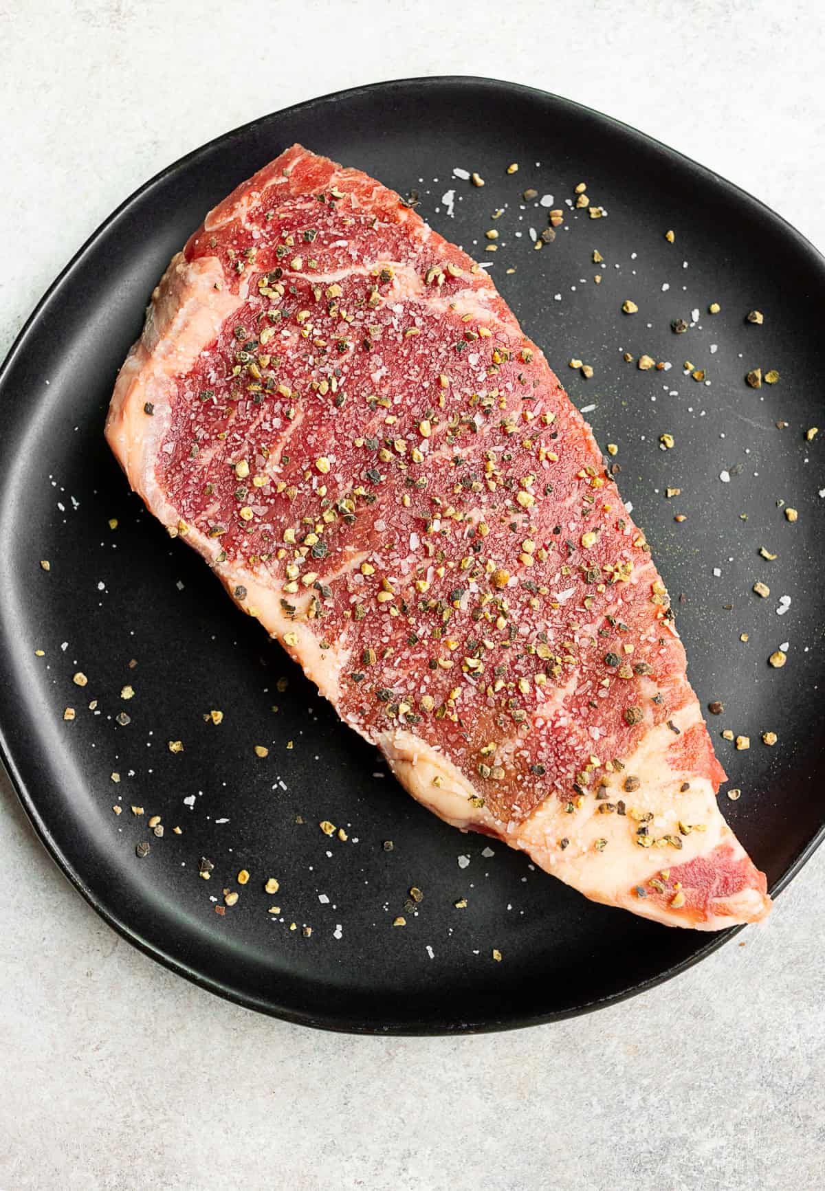 raw steak on a black plate seasoned with kosher salt and black pepper