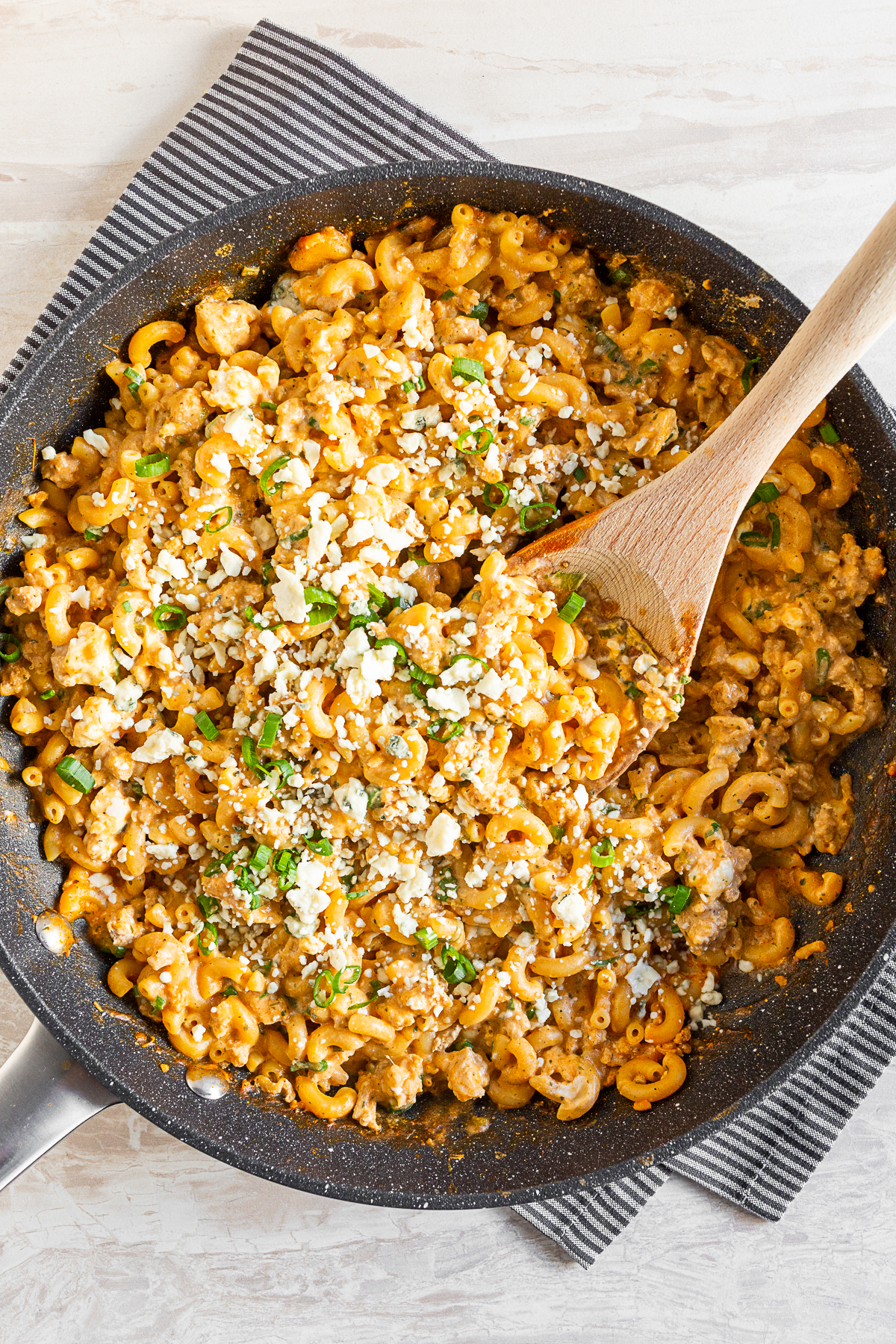 One Pot Buffalo Chicken Pasta in a skillet with a wooden spoon and topped with blue cheese. 