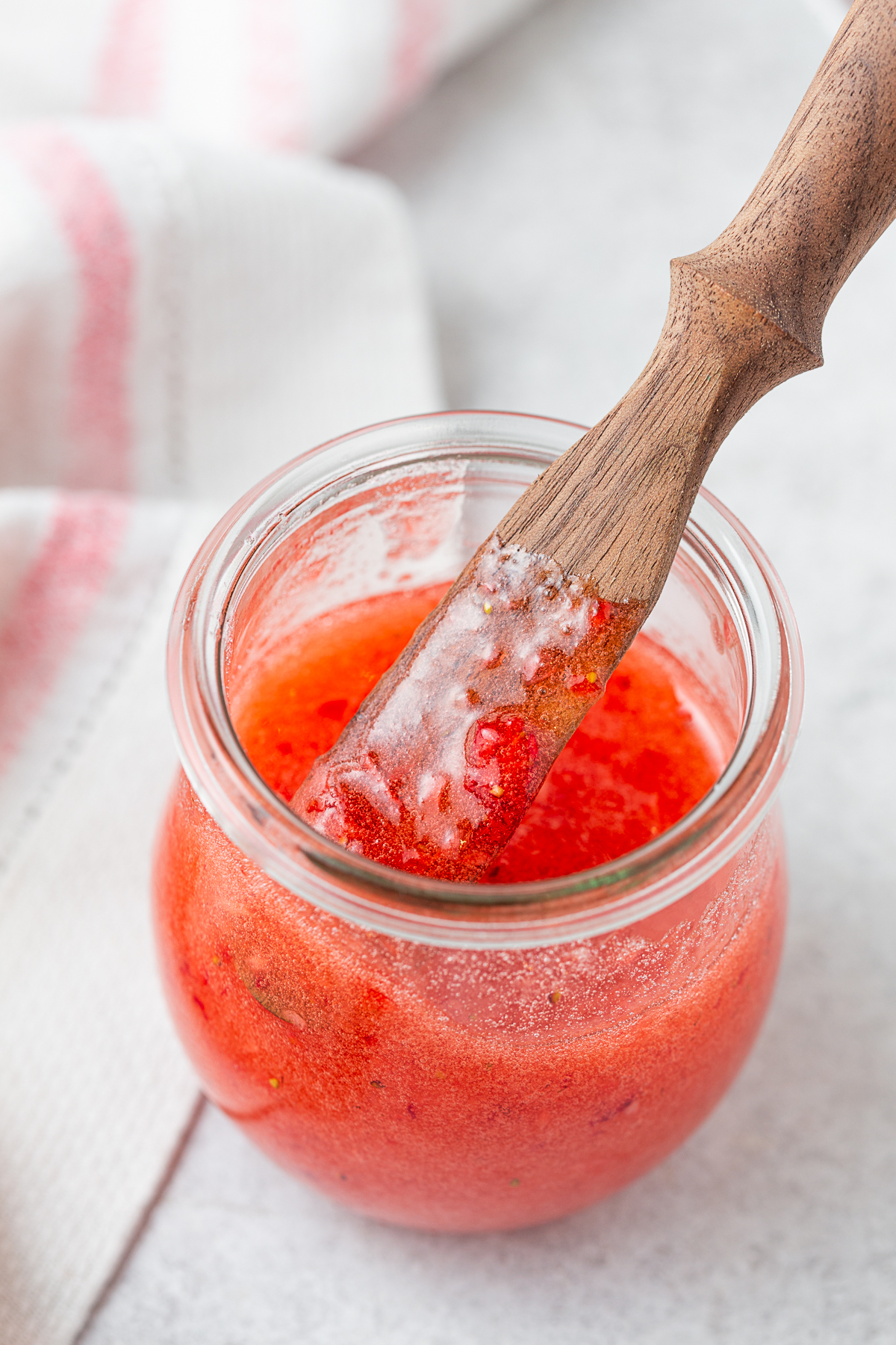A wooden knife in a jar of Strawberry Freezer Jam. 